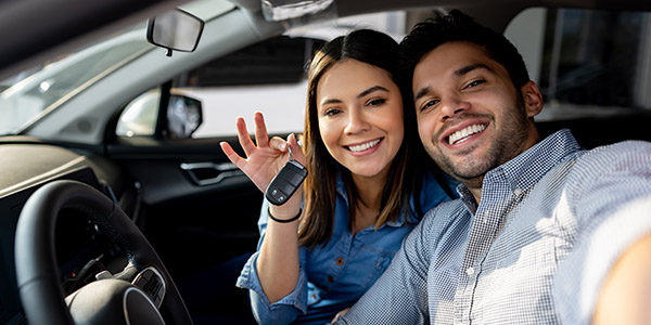 Happy couple sitting in their new car and holding the keys